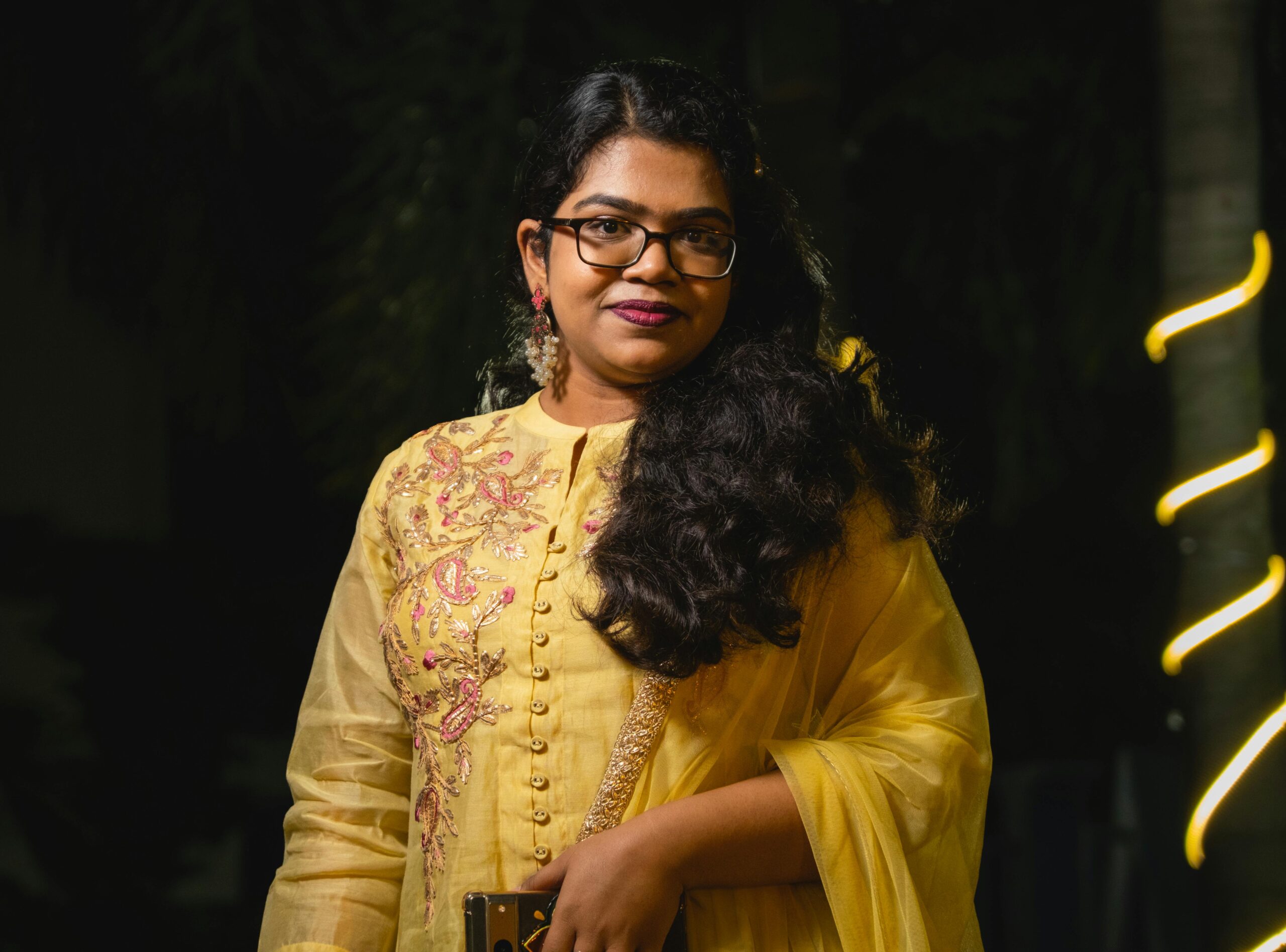 Portrait of a young woman wearing a traditional yellow outfit with embroidery, standing confidently.