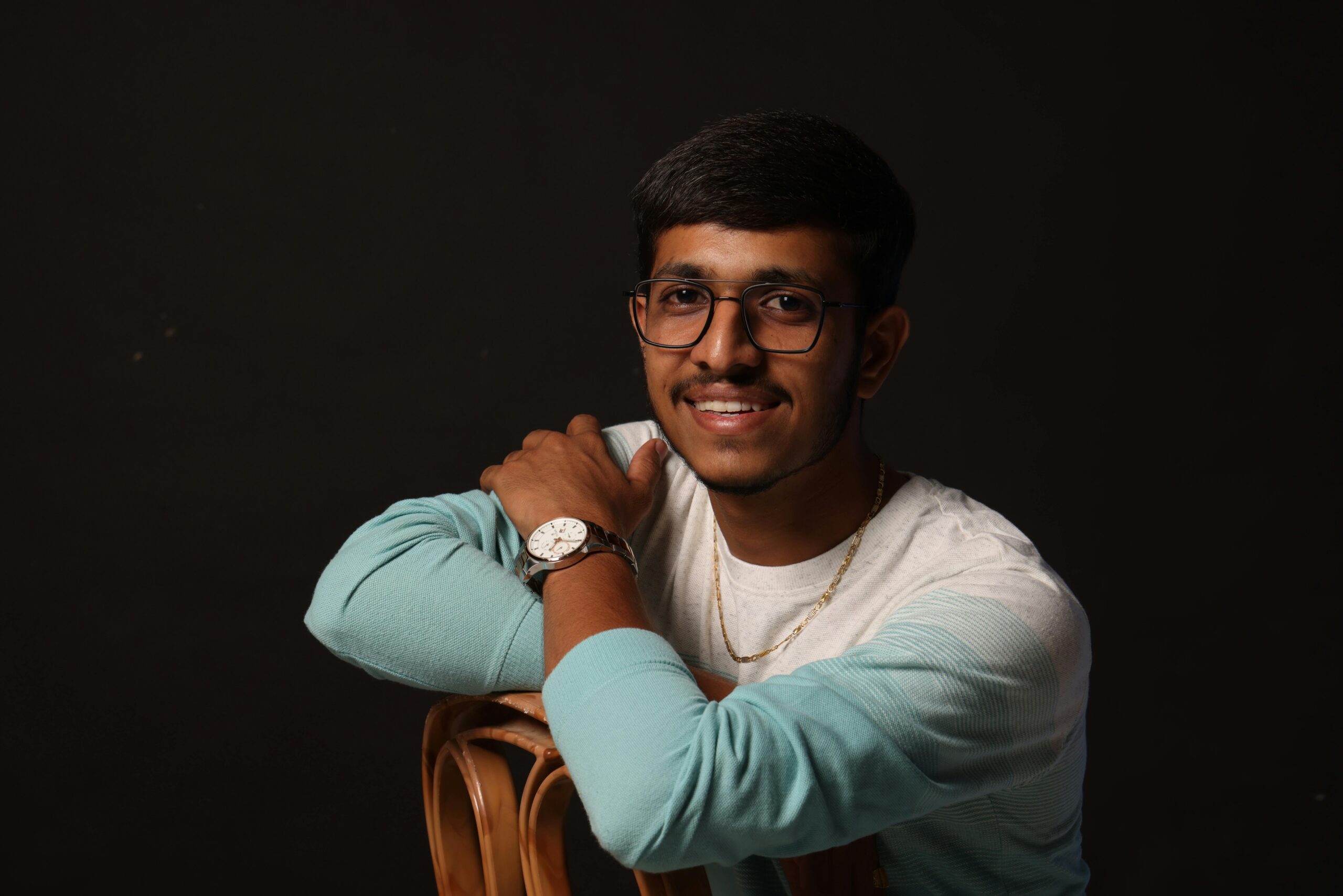 A stylish young man with glasses and a watch posing confidently in a studio setting.